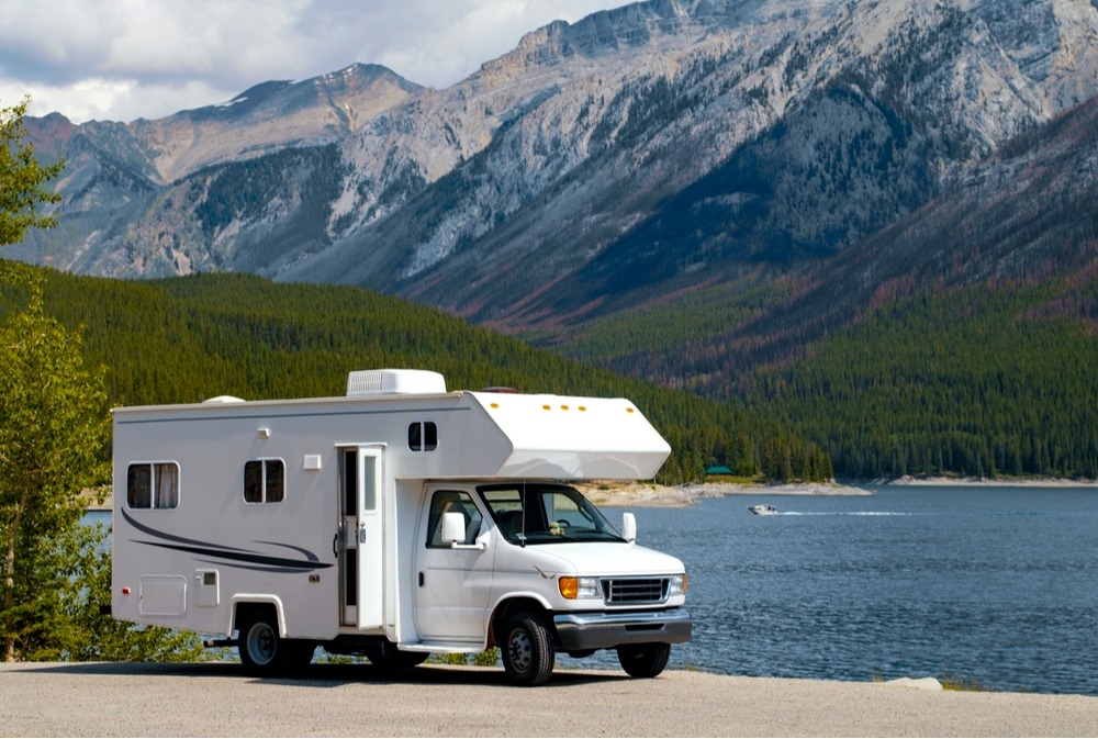 RV parked by a lake with mountains in the background.