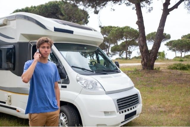 Young man with a frustrated expression talking on a cell phone in front of his RV