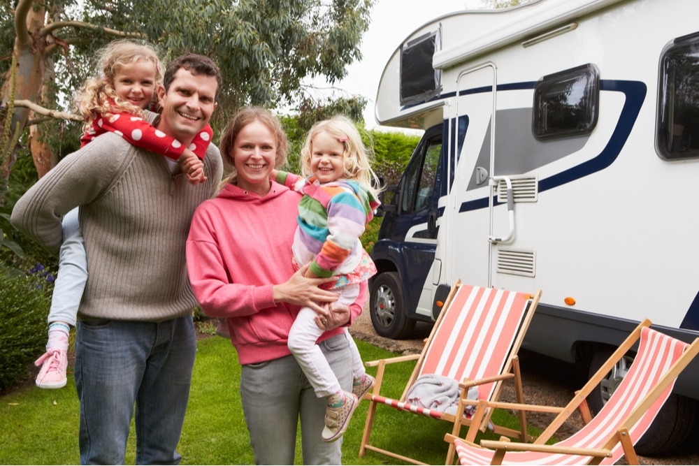 Smiling family of a mom, dad and two small children standing in front of their RV