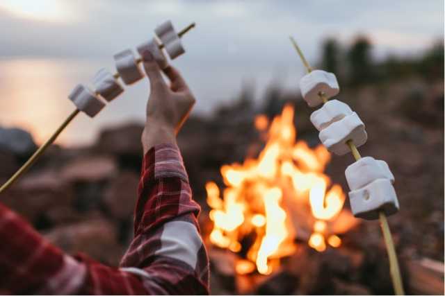 Man putting marshmallows on a skewer to roast with a fire in the background.