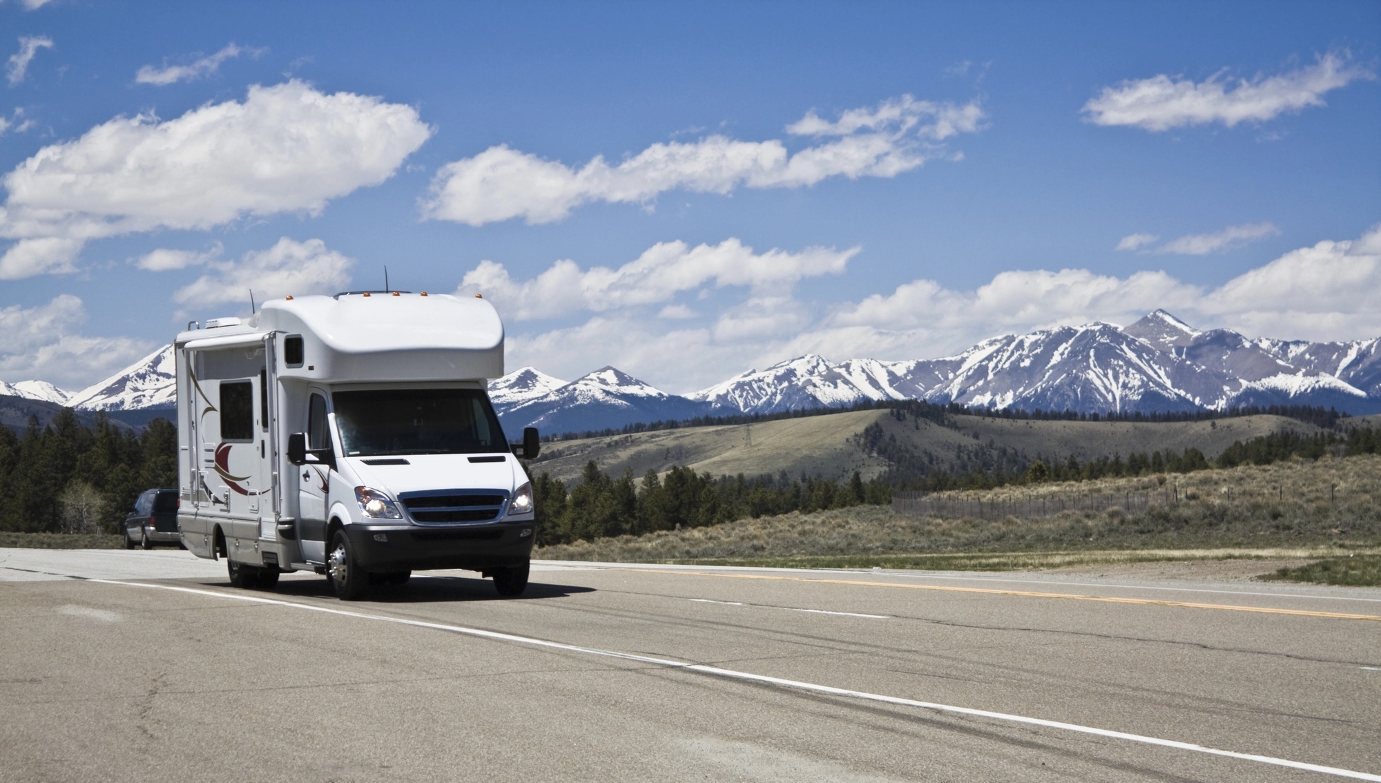 RV driving down a highway with snowy mountains in the background.