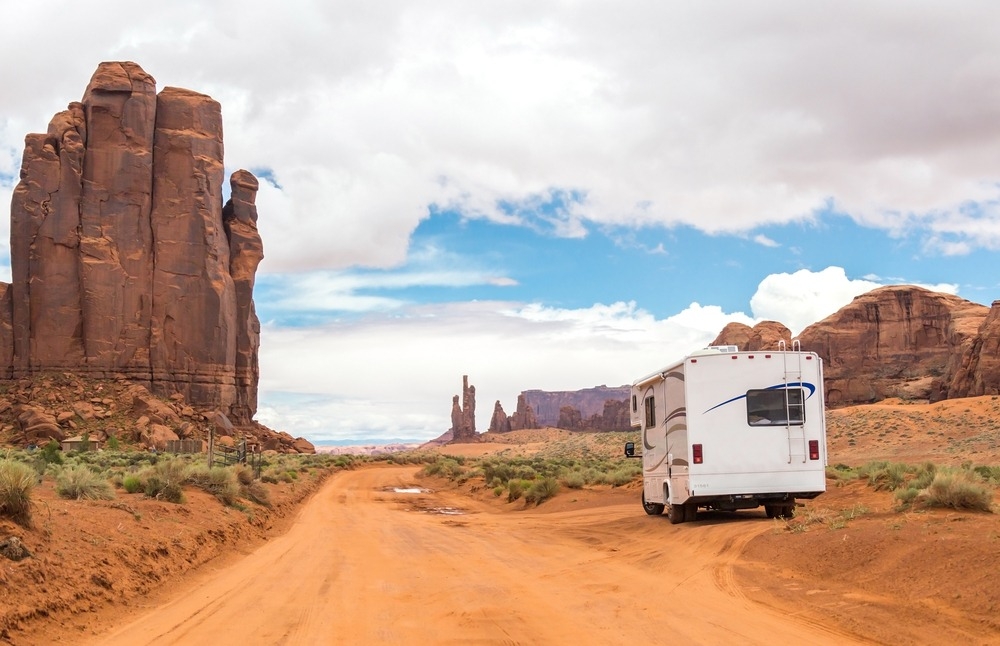 RV parked next to a scenic dirt road with sculptural red rocks.