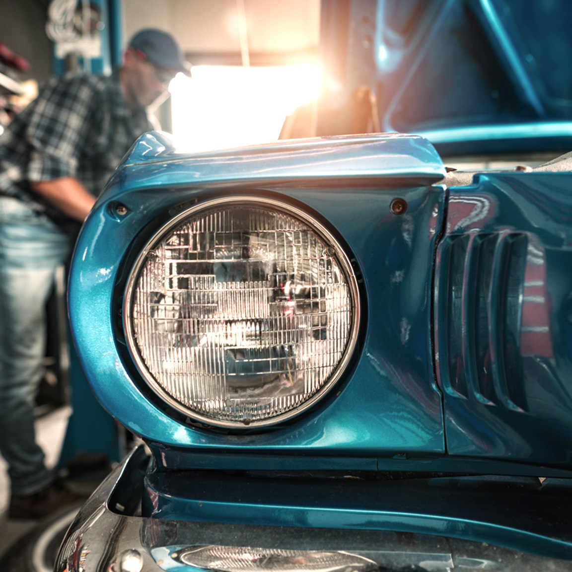 Man working on classic car in a storage unit.