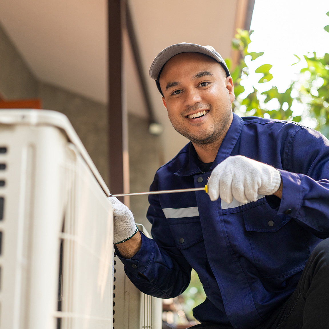 Maintenance technician smiling at the camera while working on air conditioning unit.