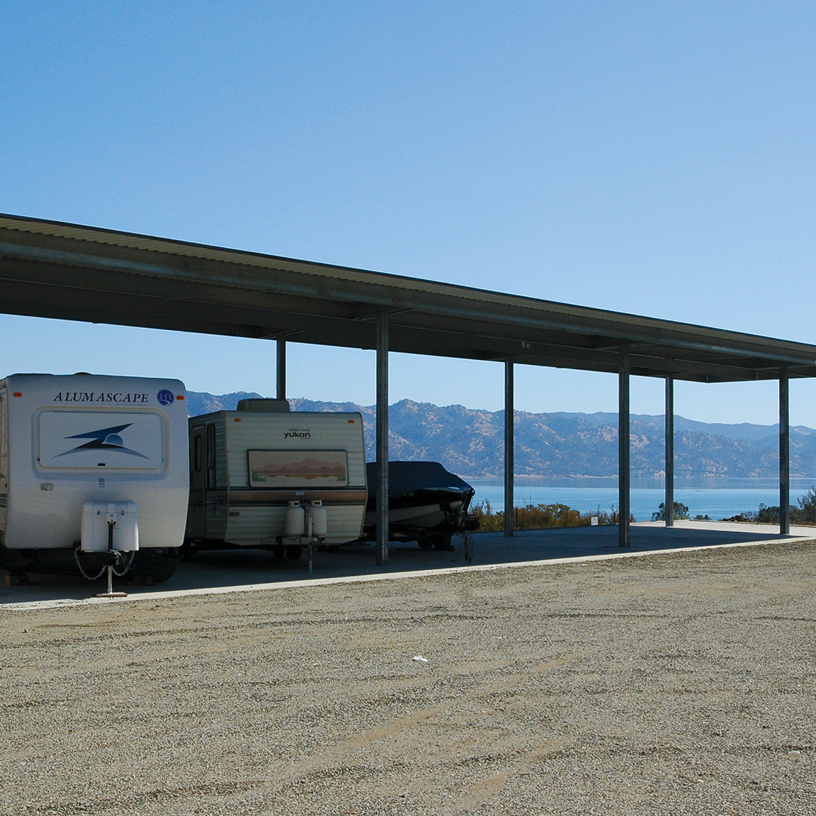 Two RVs and a boat under canopy storage near a lake.
