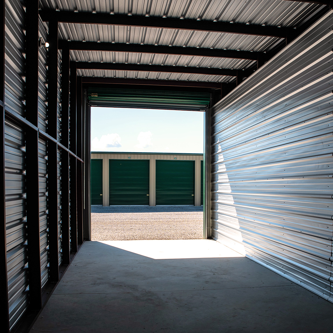 Image shot from interior of large garage unit, looking out at driveway and other closed garages.